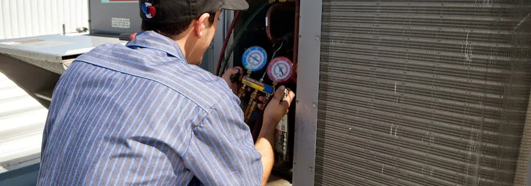 HVAC technician servicing a condenser unit in Harahan